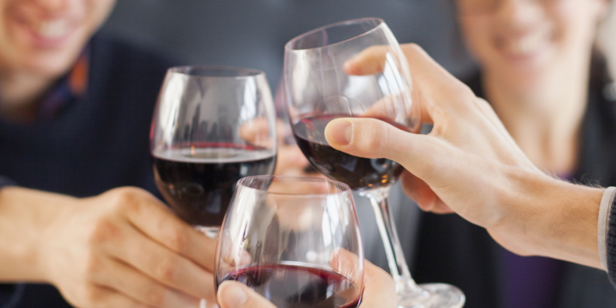 Happy friends toasting red wine glasses at restaurant table