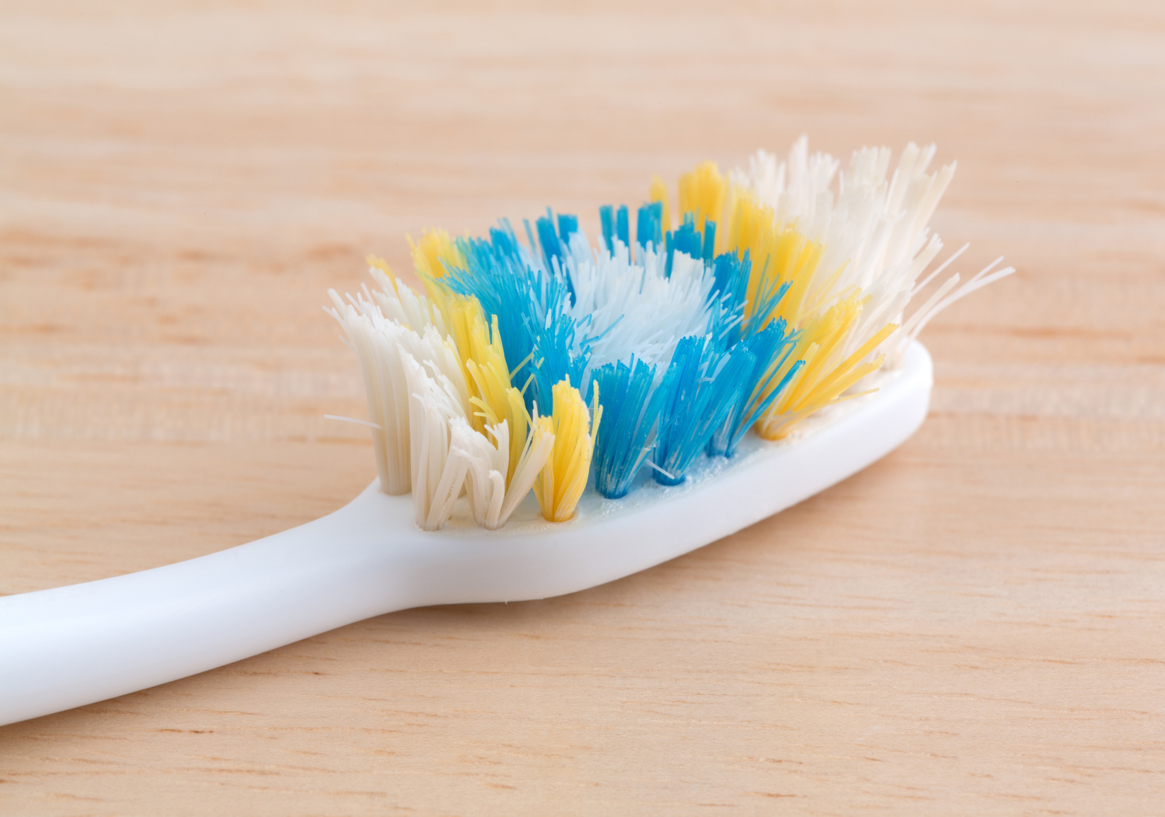 An old worn toothbrush with bent bristles on a wood counter top illuminated with natural light.