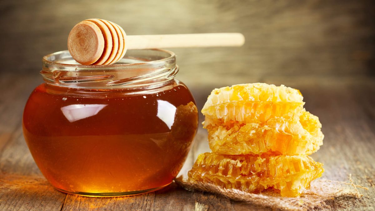 jar of honey with honeycomb on wooden table