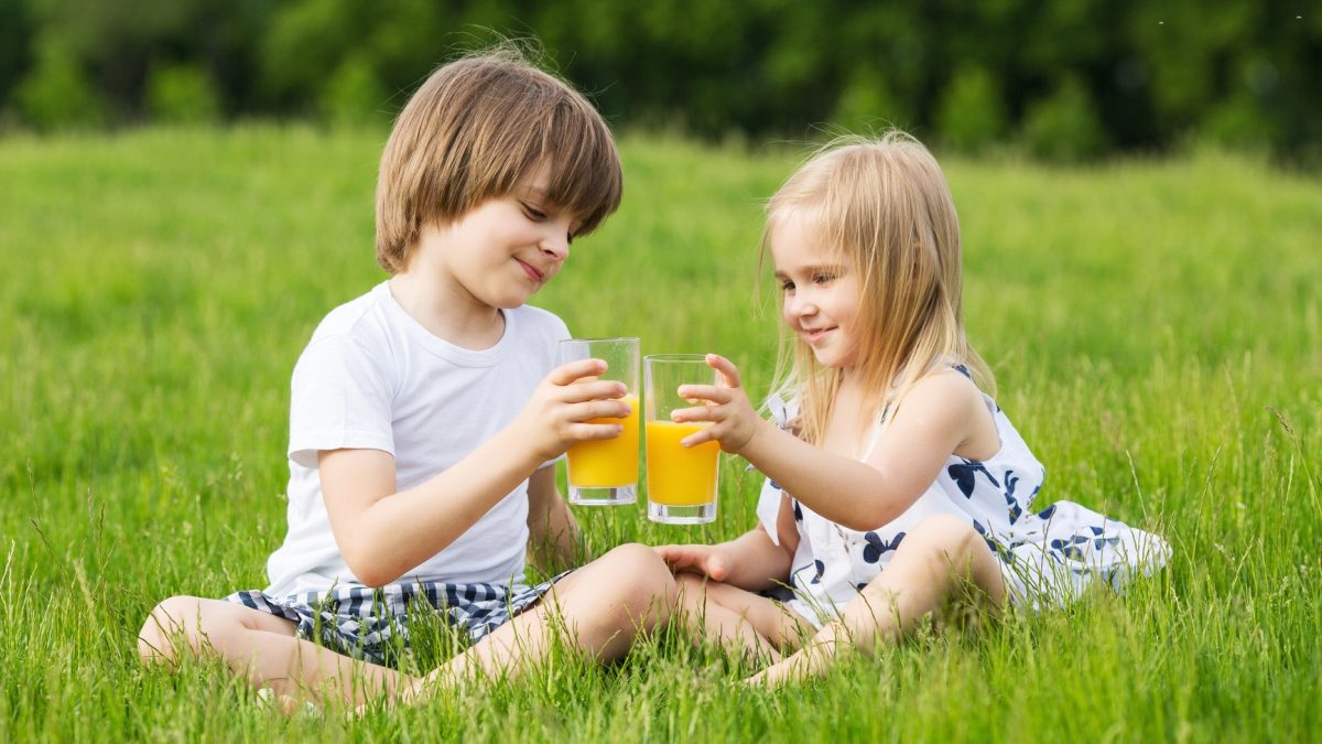 Little girl and boy outdoor summer drink juice