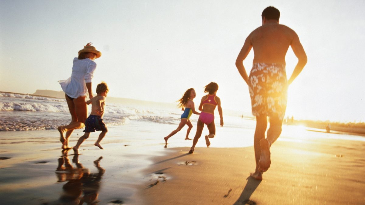 Family running on beach at sunset, rear view
